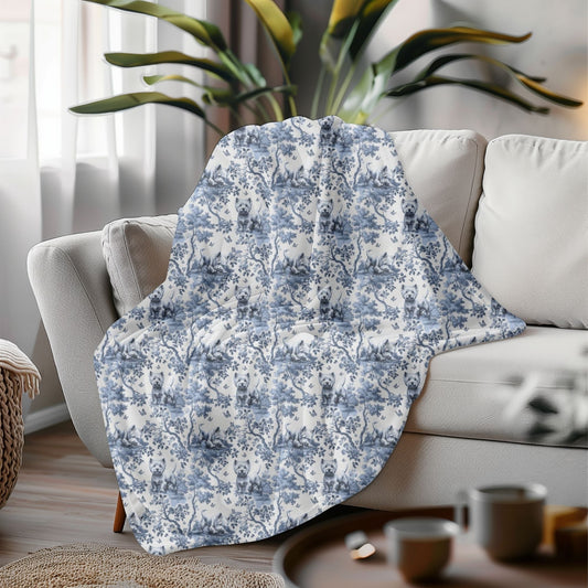 Westie blanket with a beautiful blue toile de jouy pattern on a grey couch in a living room with a plant in the background.