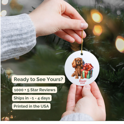 Hand holding a personalized Ruby Cavalier King Charles Spaniel ceramic ornament beside a Christmas tree