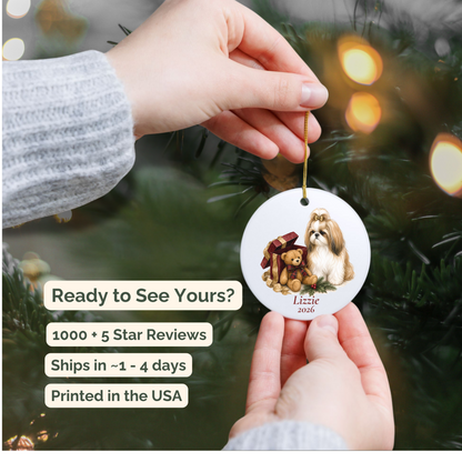 Hand holding a personalized Shih Tzu wearing a bow ceramic ornament beside a Christmas tree