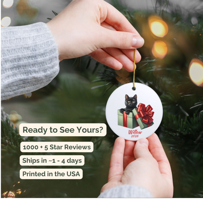 Hand holding a personalized Black Cat ceramic ornament beside a Christmas tree