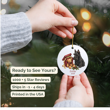 Hand holding a personalized Scottish Terrier ceramic ornament beside a Christmas tree