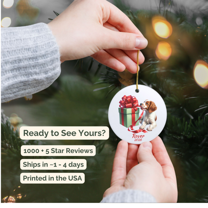 Hand holding a personalized Brittany Spaniel ceramic ornament beside a Christmas tree