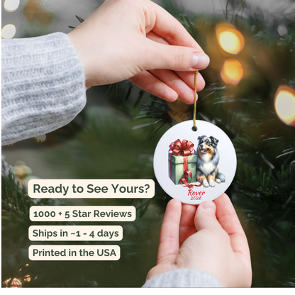 Hand holding a personalized Australian Shepherd ceramic ornament beside a Christmas tree
