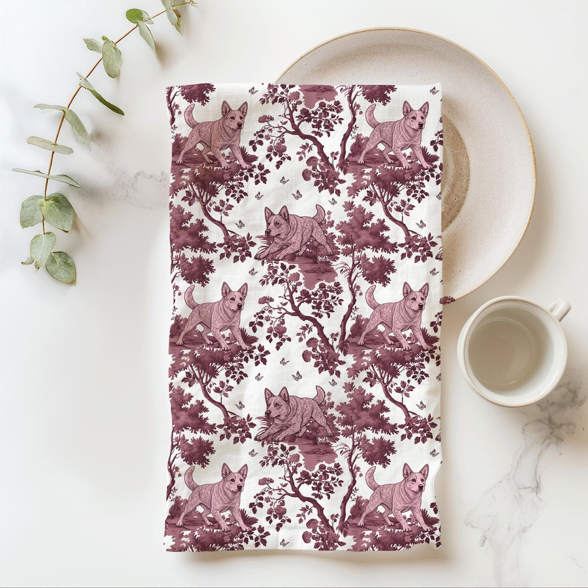 Australian Cattle Dog Red Tea Towel with cranberry toile design, folded beside a plate and cup.
