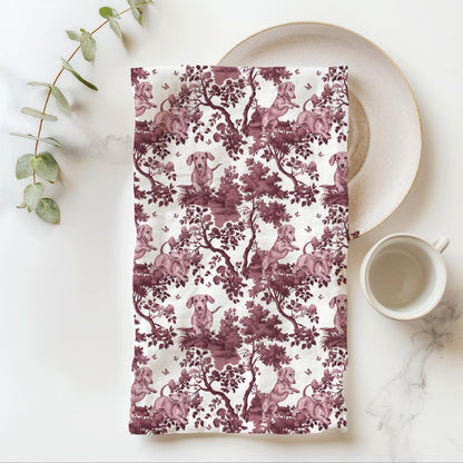 Dachshund Tea Towel with cranberry toile design, folded beside a plate and cup.