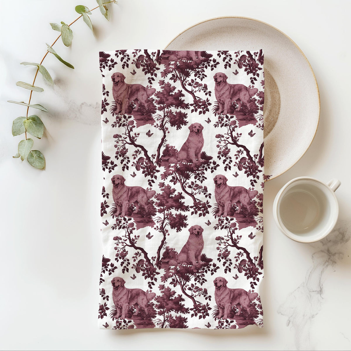 Golden Retriever Tea Towel with cranberry toile design, folded beside a plate and cup.