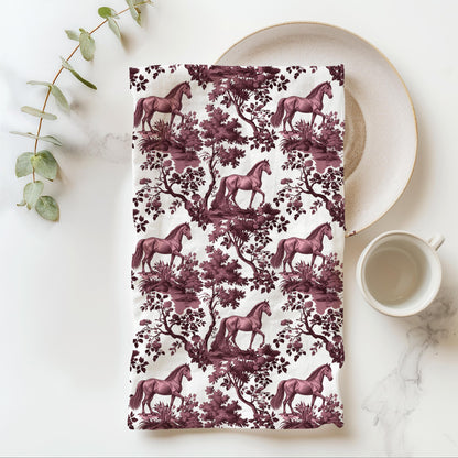 Horse Tea Towel with cranberry toile design, folded beside a plate and cup.