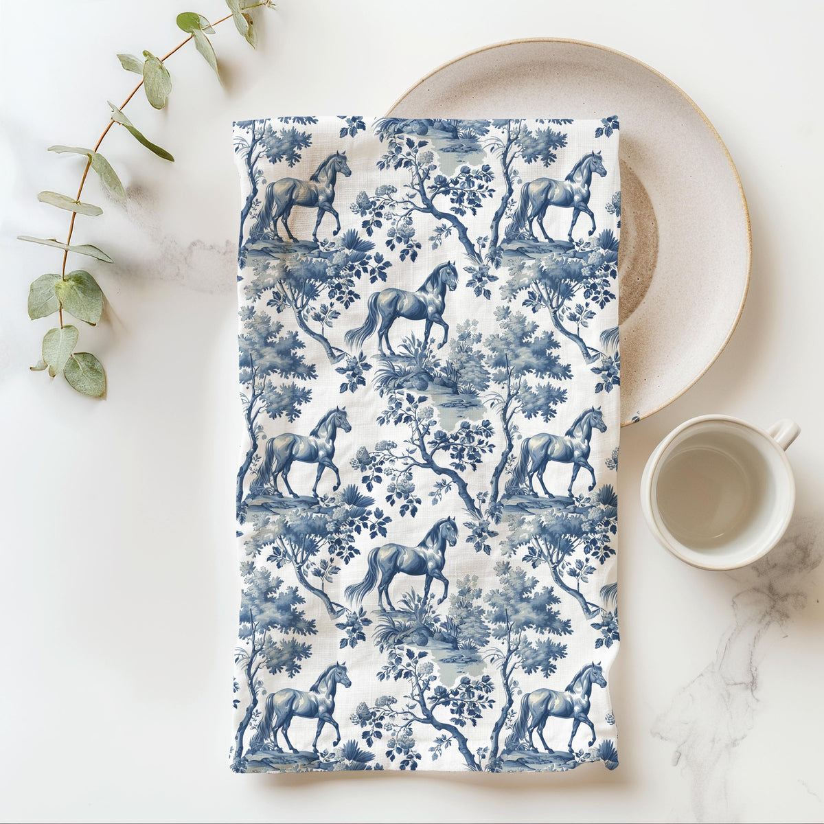 Horse Tea Towel with blue toile design, folded beside a plate and cup.