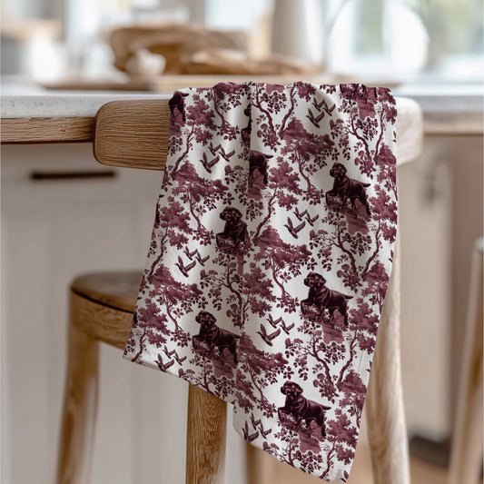 Black Labrador Duck Tea Towel with cranberry toile design, draped over a wooden chair in a kitchen.