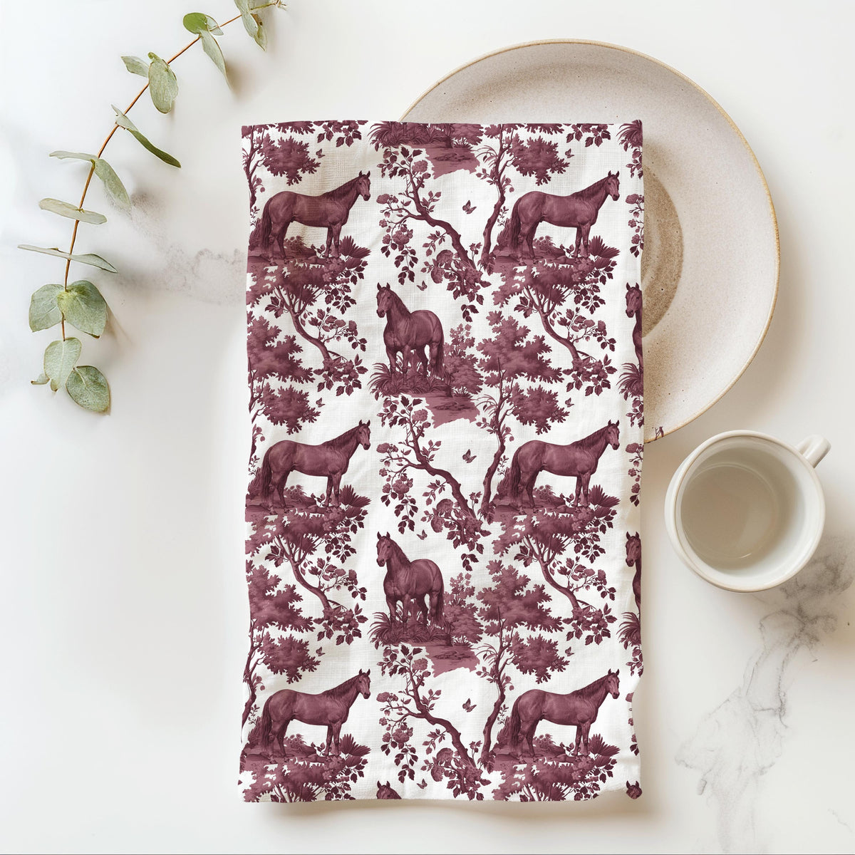 Quarter Horse Tea Towel with cranberry toile design, folded beside a plate and cup.