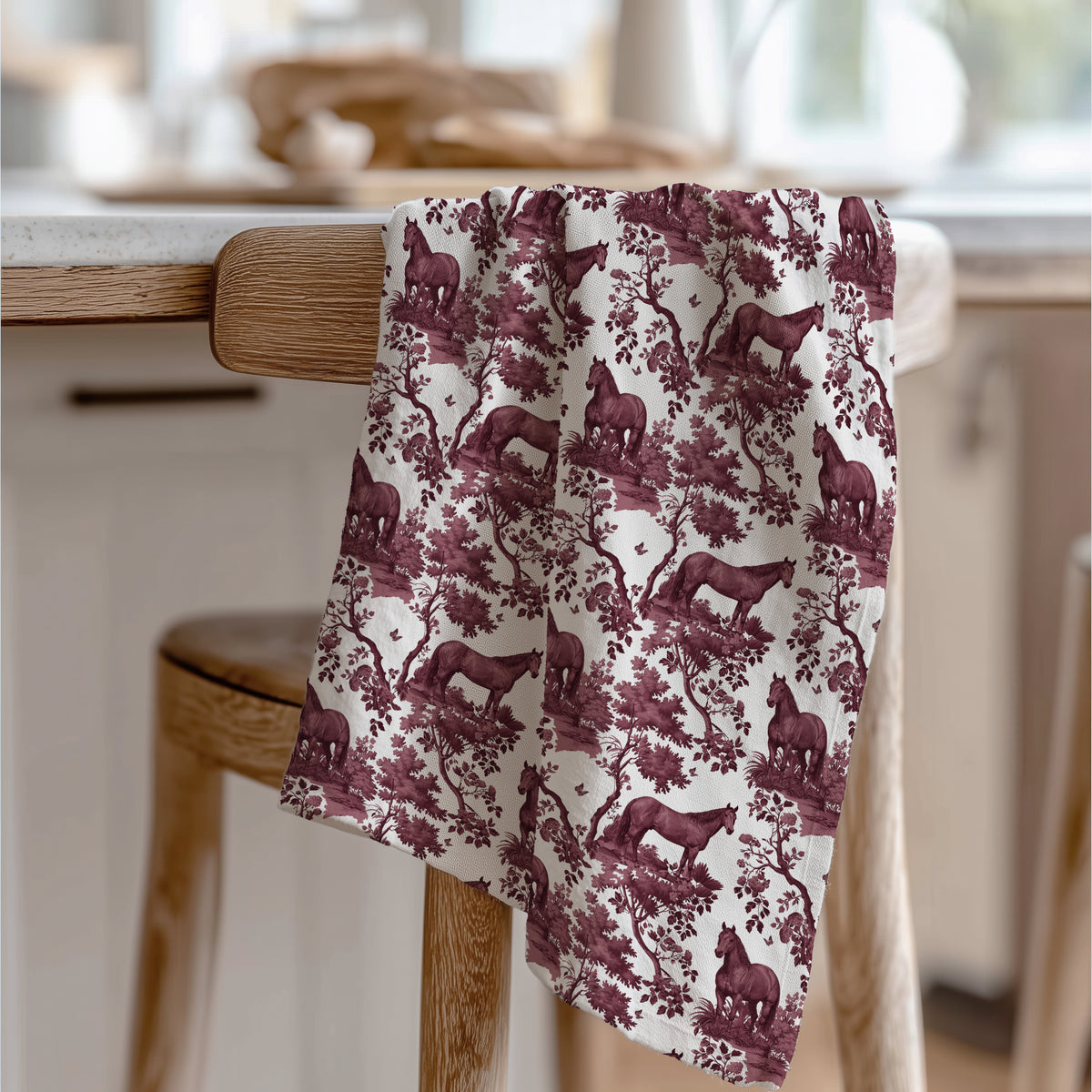 Quarter Horse Tea Towel with cranberry toile design, draped over a wooden chair in a kitchen.