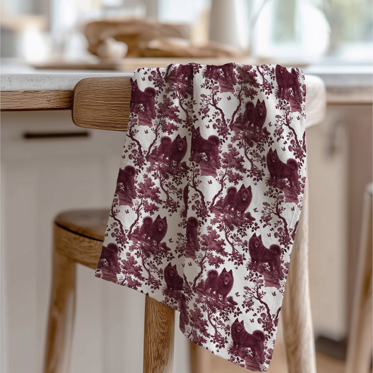Schipperke Tea Towel with cranberry toile design, draped over a wooden chair in a kitchen.