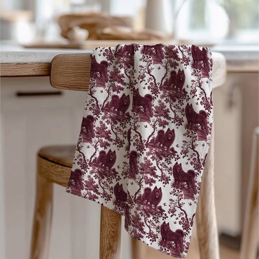 Schipperke Tea Towel with cranberry toile design, draped over a wooden chair in a kitchen.