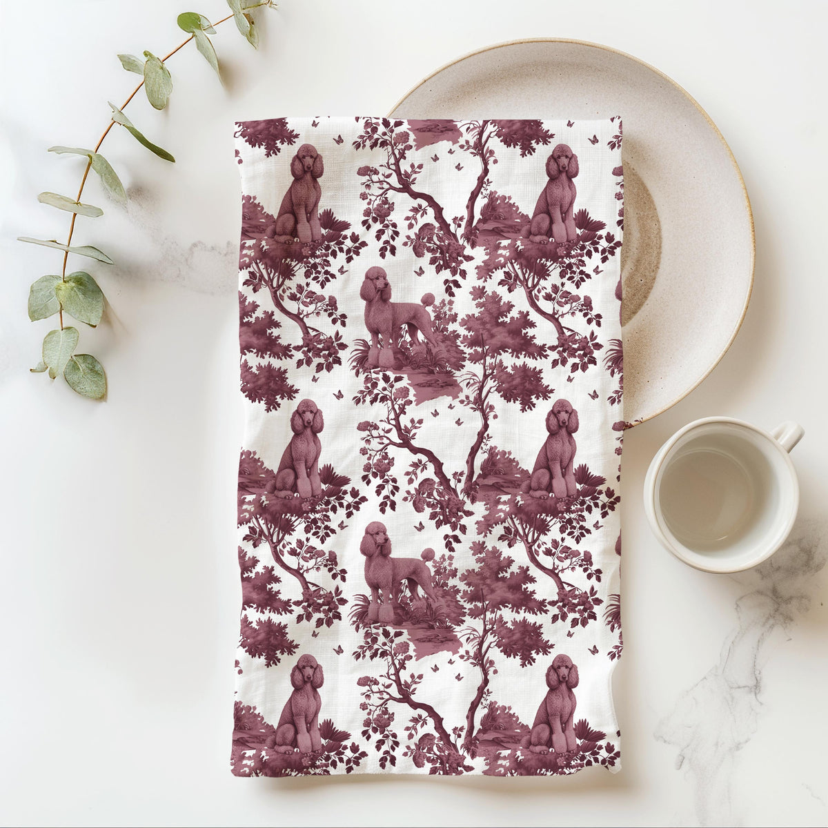 Standard Poodle Tea Towel with cranberry toile design, folded beside a plate and cup.