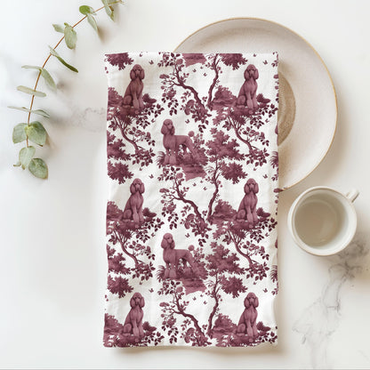Standard Poodle Tea Towel with cranberry toile design, folded beside a plate and cup.