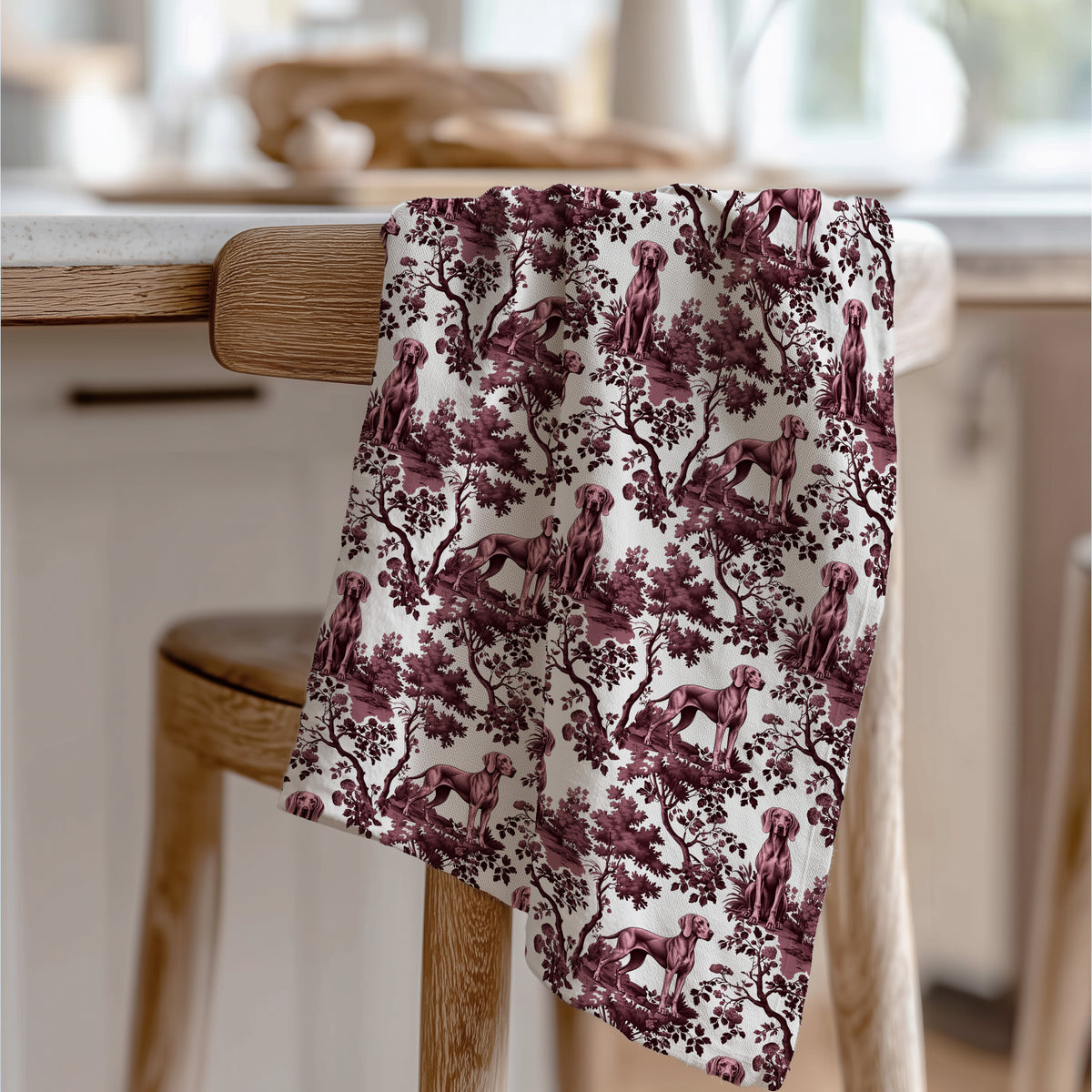 Weimaraner Tea Towel with cranberry toile design, draped over a wooden chair in a kitchen.