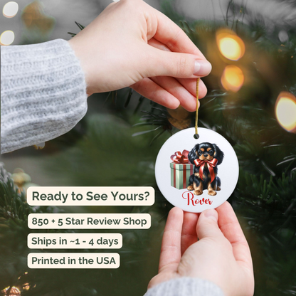 Hand holding a Christmas ornament with a Cavalier King Charles Spaniel dog design against a festive background. 850 + 5 Star Review Shop. Ships in ~ 1 to 4 days. Printed in the USA.