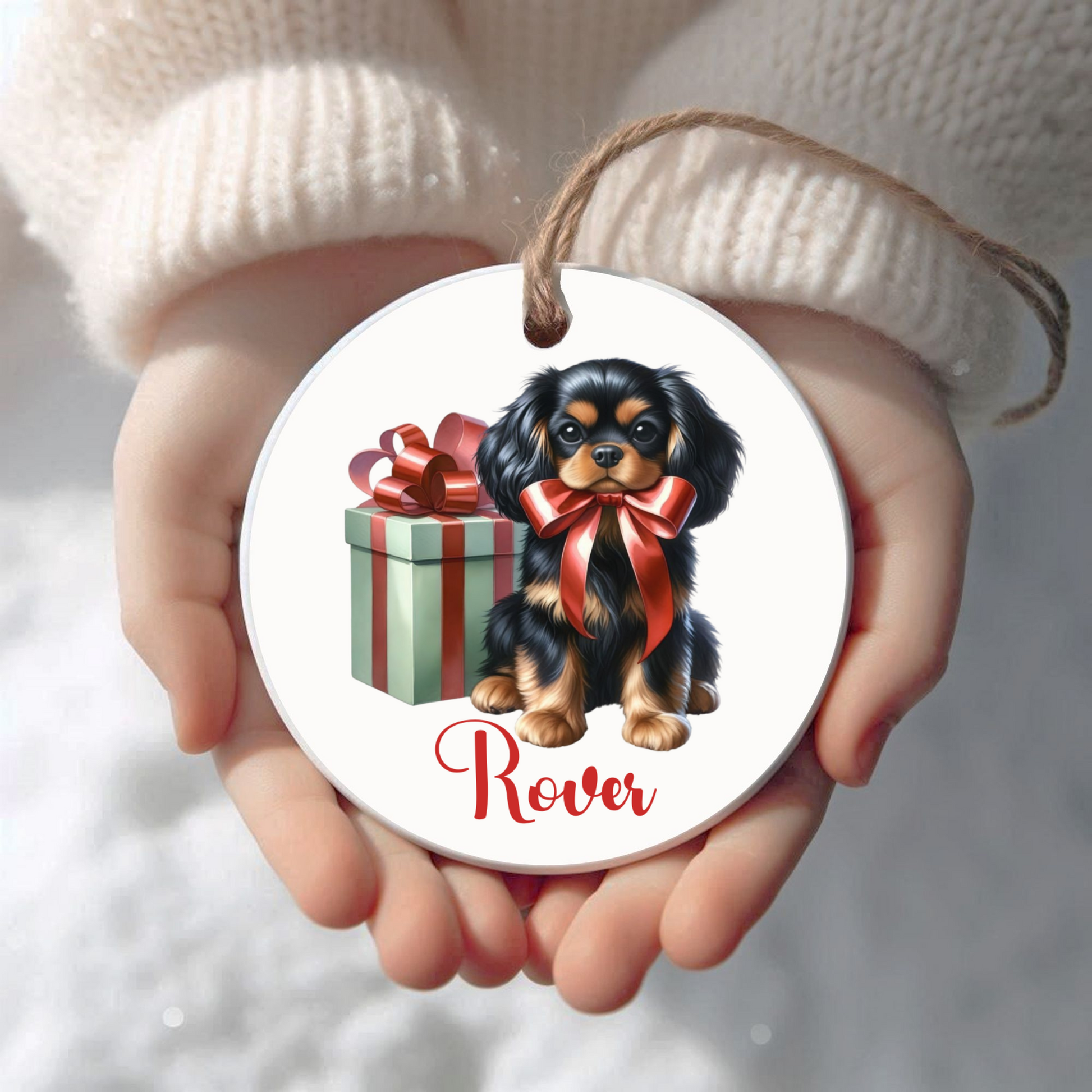 Round Christmas ceramic ornament with a Cavalier King Charles Spaniel dog illustration and gift, held in hands against a white background