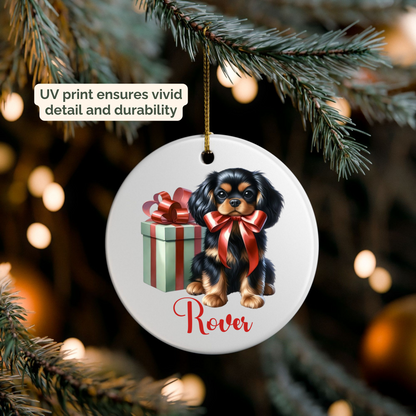 Christmas ornament with a Cavalier King Charles Spaneil dog and gift box design, hanging on a tree branch. Ornament is UV printed to ensure detail and durability.
