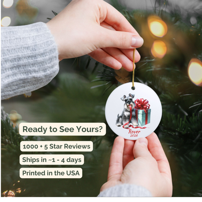 Hand holding a personalized Miniature Schnauzer ceramic ornament beside a Christmas tree
