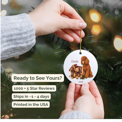 Hand holding a personalized Standard Poodle ceramic ornament beside a Christmas tree