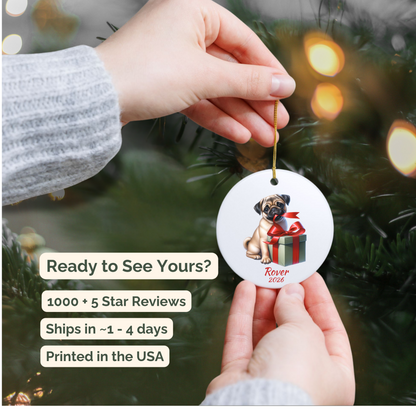 Hand holding a personalized fawn Pug ceramic ornament beside a Christmas tree
